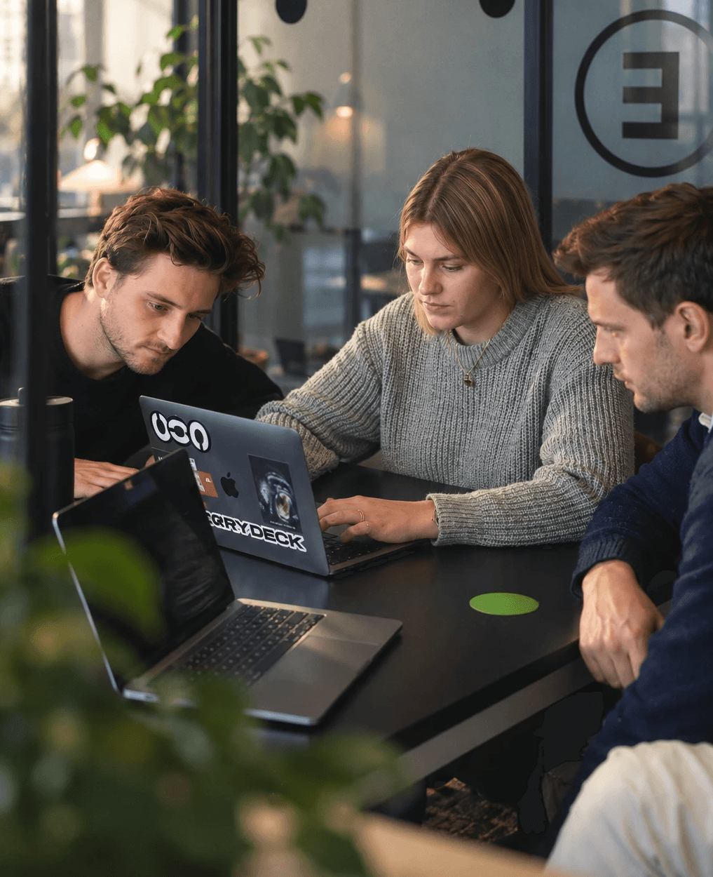 Three people collaborating on a laptop at a black table in an office